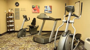 Ein Fitnessraum mit Laufbändern und einem Crosstrainer, einer Uhr und einem Wandkorb mit Handtüchern.