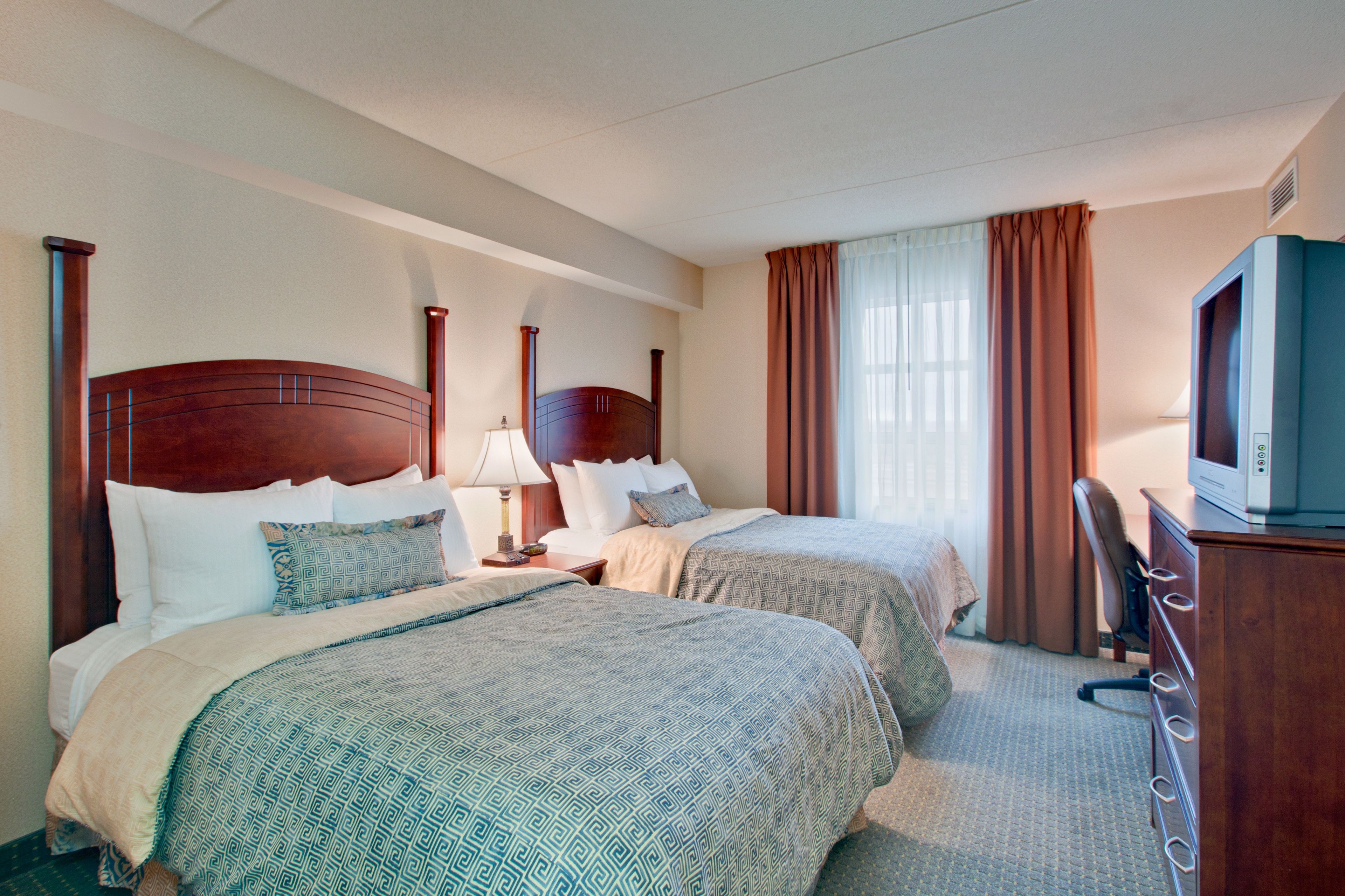 A hotel room with two beds, a desk, a television, and a window with curtains.
