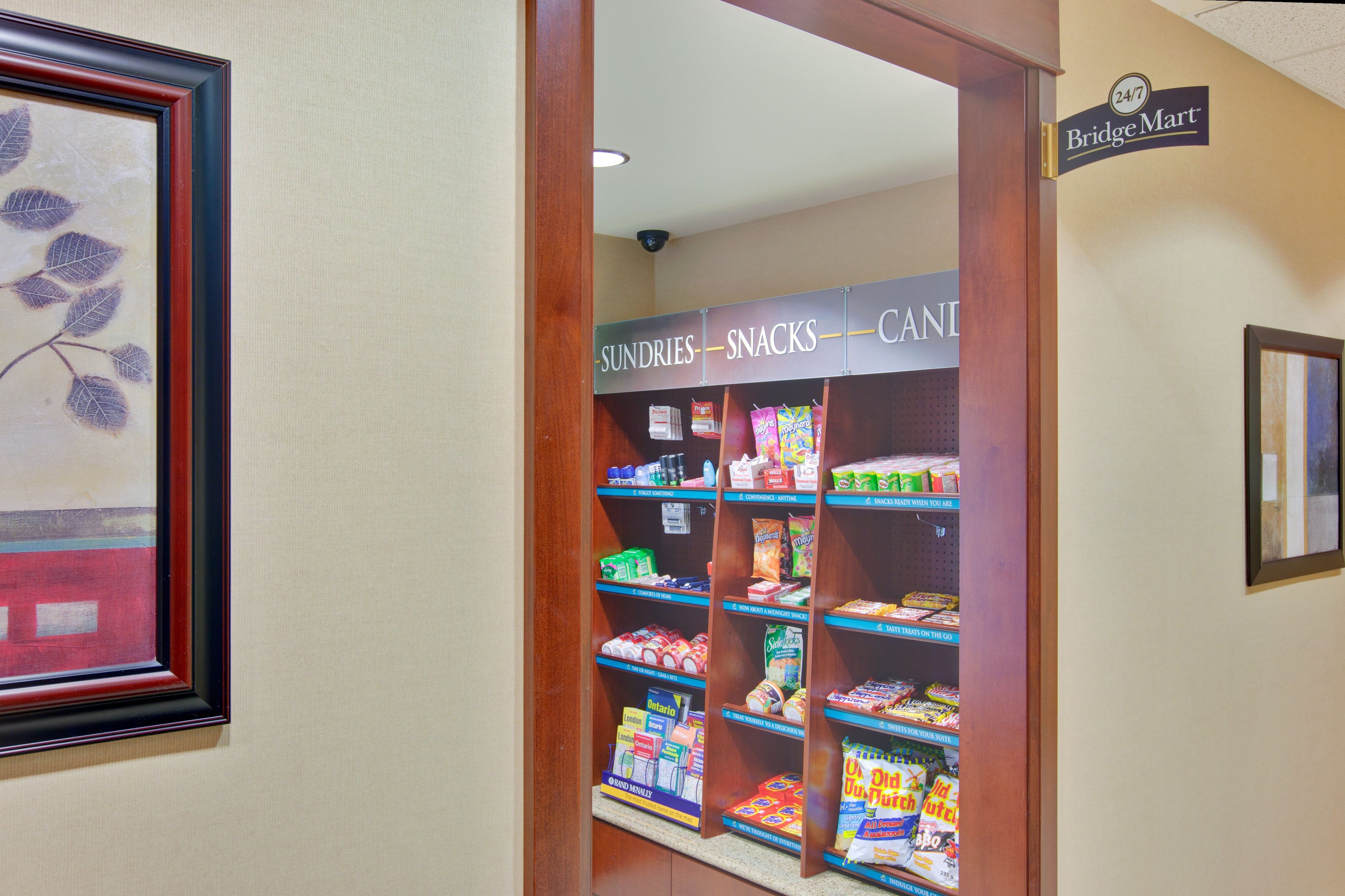 A hallway with a framed artwork on the left and a snack display with various products on the right.
