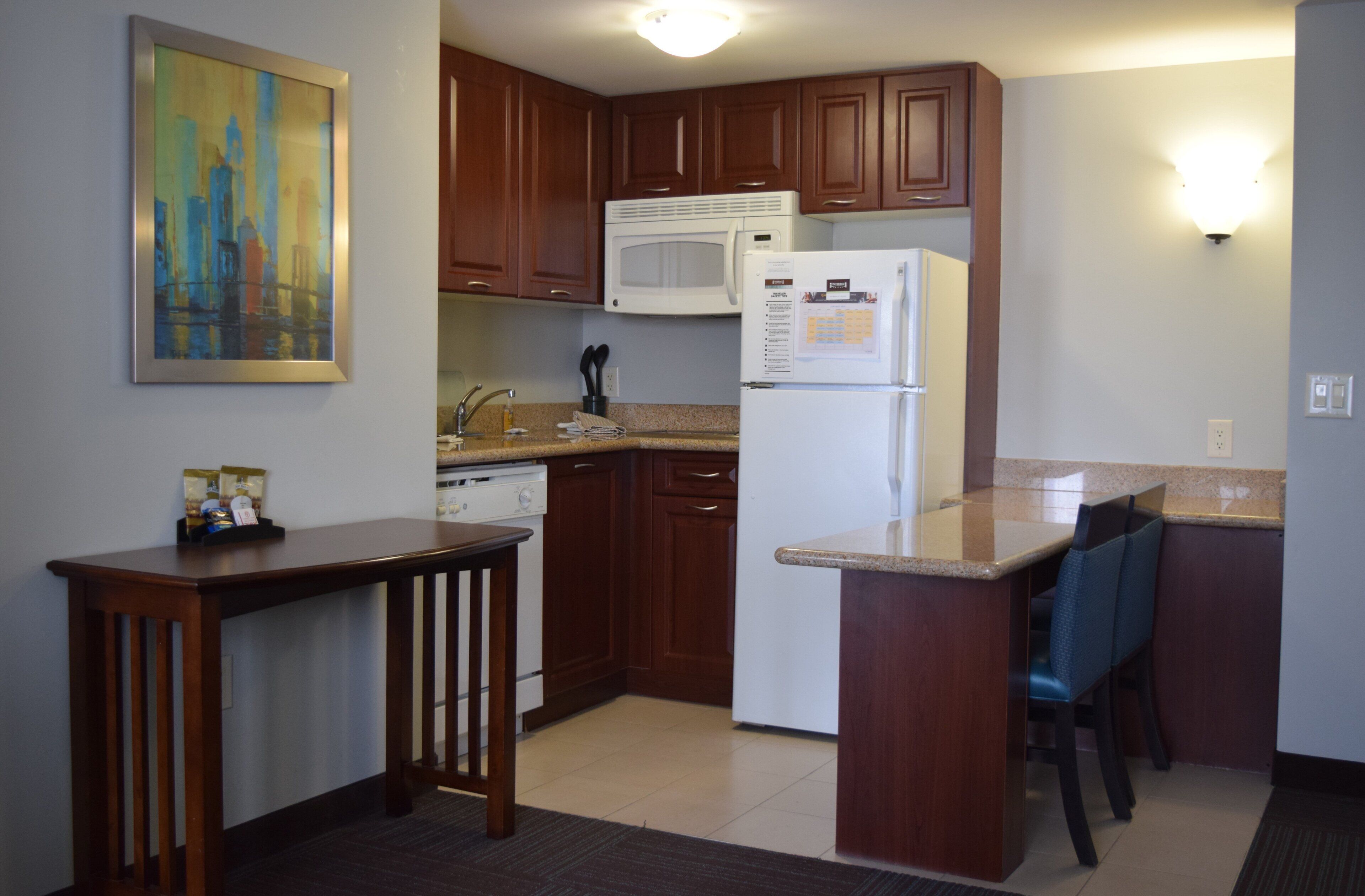 A kitchen with wooden cabinets, a microwave, a refrigerator, and a painting on the wall.