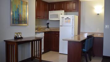 A kitchen with wooden cabinets, a microwave, a refrigerator, and a painting on the wall.