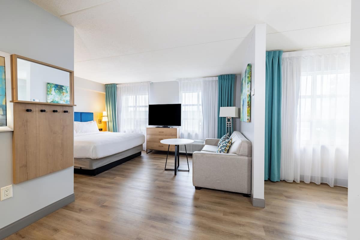 A hotel room with a bed, a sofa, a TV, a small table, and a mirror.