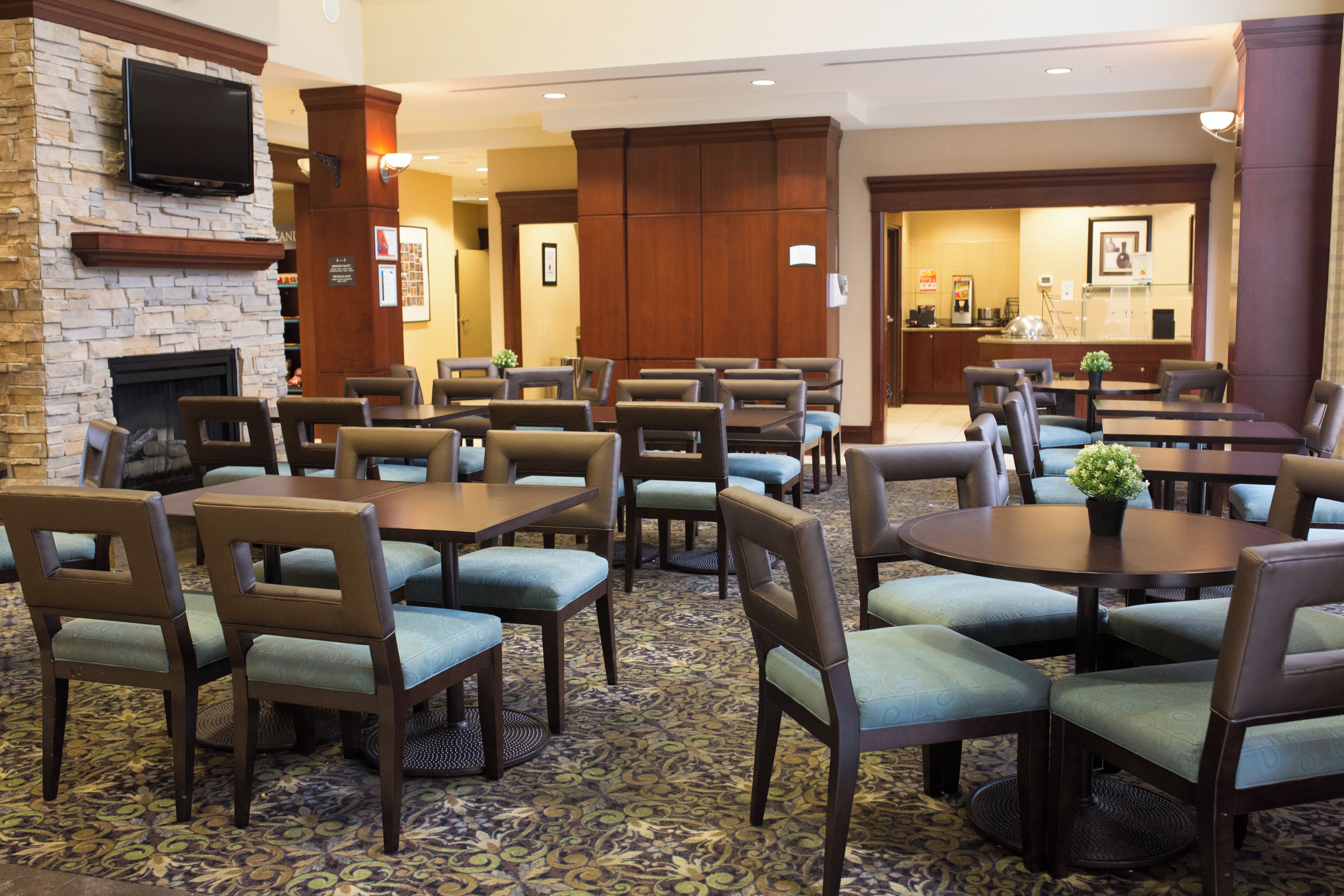 Une salle à manger d’hôtel avec plusieurs tables et chaises, une cheminée et un téléviseur fixé au mur.