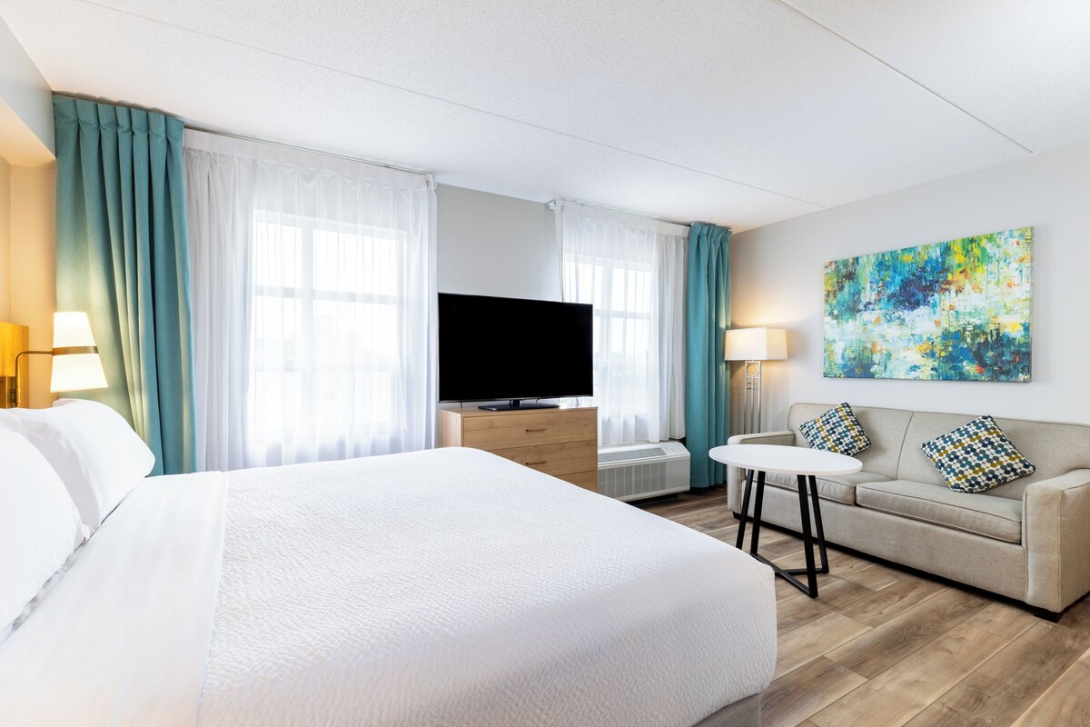 Een hotelkamer met een groot bed, een televisie, een bank en een schilderij aan de muur.