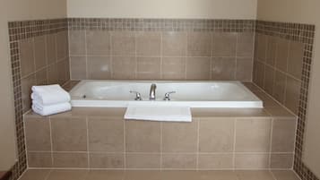 A standard hotel bathroom with a bathtub, two faucets, and a stack of white towels.