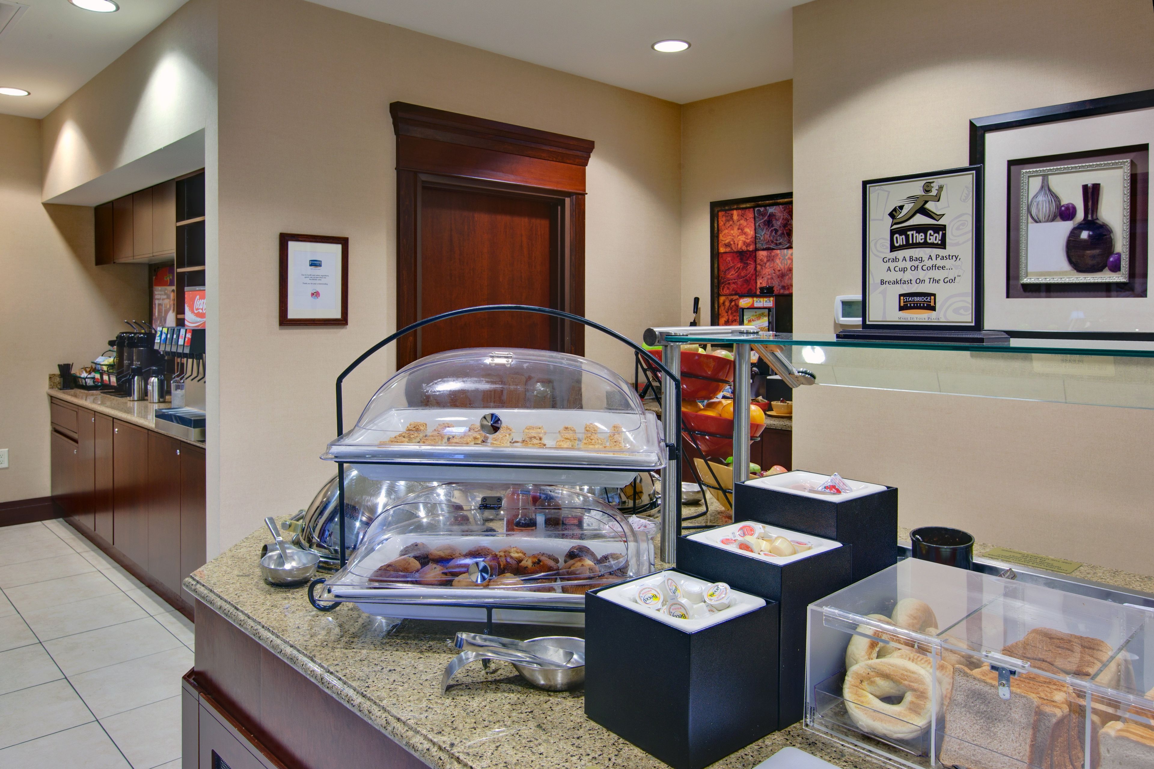 Espaço do buffet de café da manhã com diversos alimentos, uma máquina de café e quadros nas paredes.