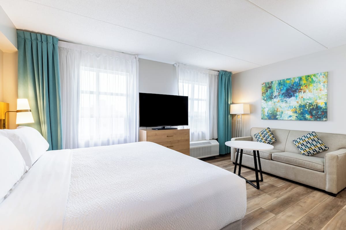 A hotel room with a large bed, a television, a sofa, and a small table.