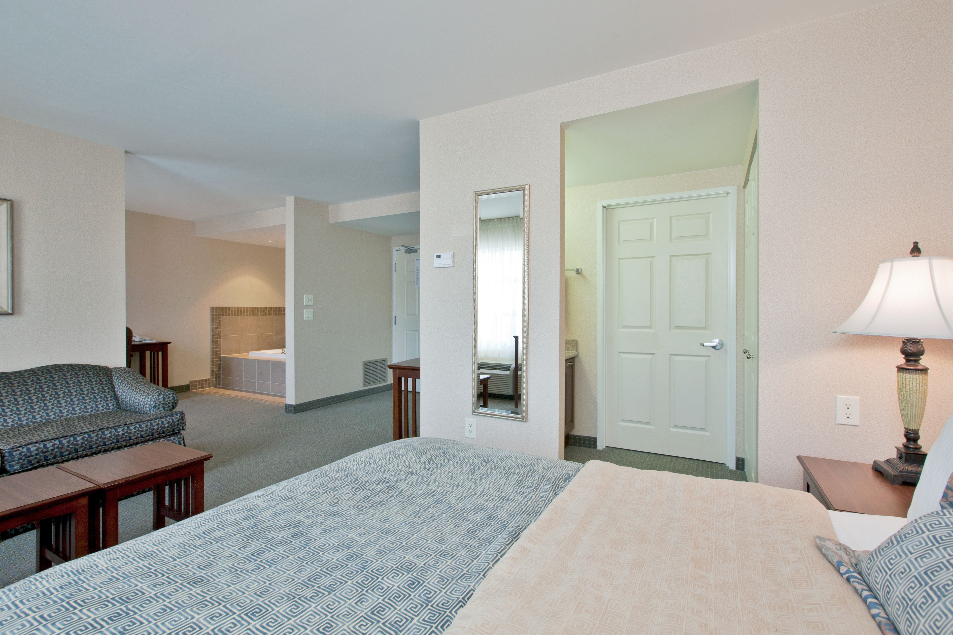 Habitación de hotel con cama, sofá, escritorio, lámpara y baño visible a través de una puerta abierta.