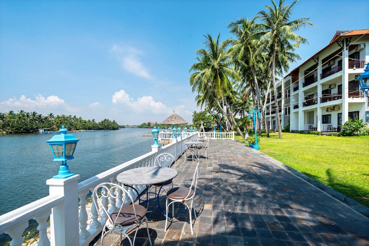 A waterfront hotel with outdoor seating, palm trees, and a view of the water.