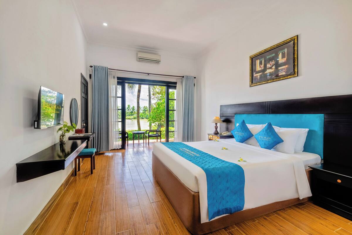 A hotel room with a large bed, a desk with a chair, a TV, and a view of the outdoors.