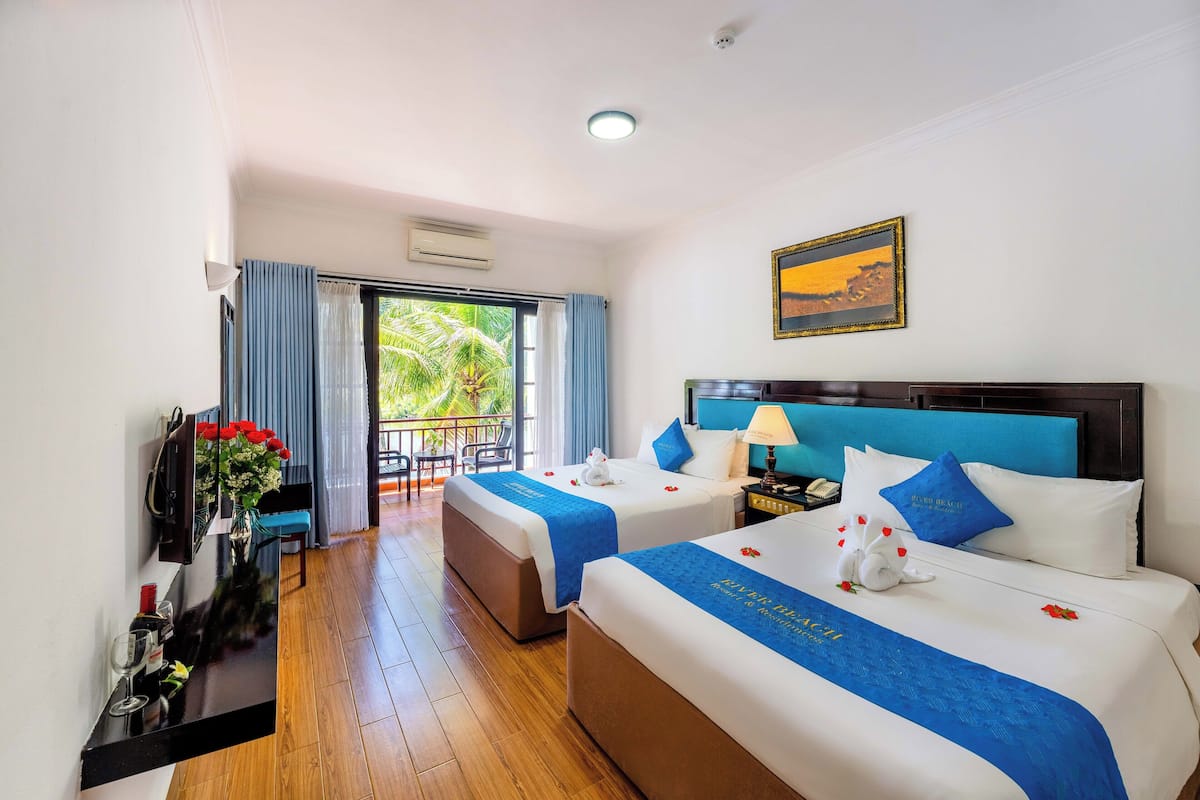 A hotel room with two beds, a balcony, a desk with a vase of flowers, and a painting on the wall.