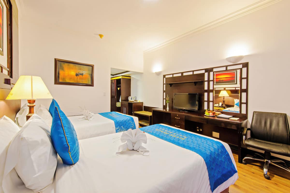 A hotel room with two beds, a desk, a TV, and a chair.