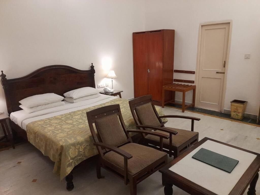 A bedroom with a bed, two chairs, a table, a wardrobe, and a door.