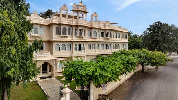 A large, ornate building with multiple balconies and arched windows, surrounded by lush greenery. - Rampratap Palace By Fateh Collection (Udaipur)