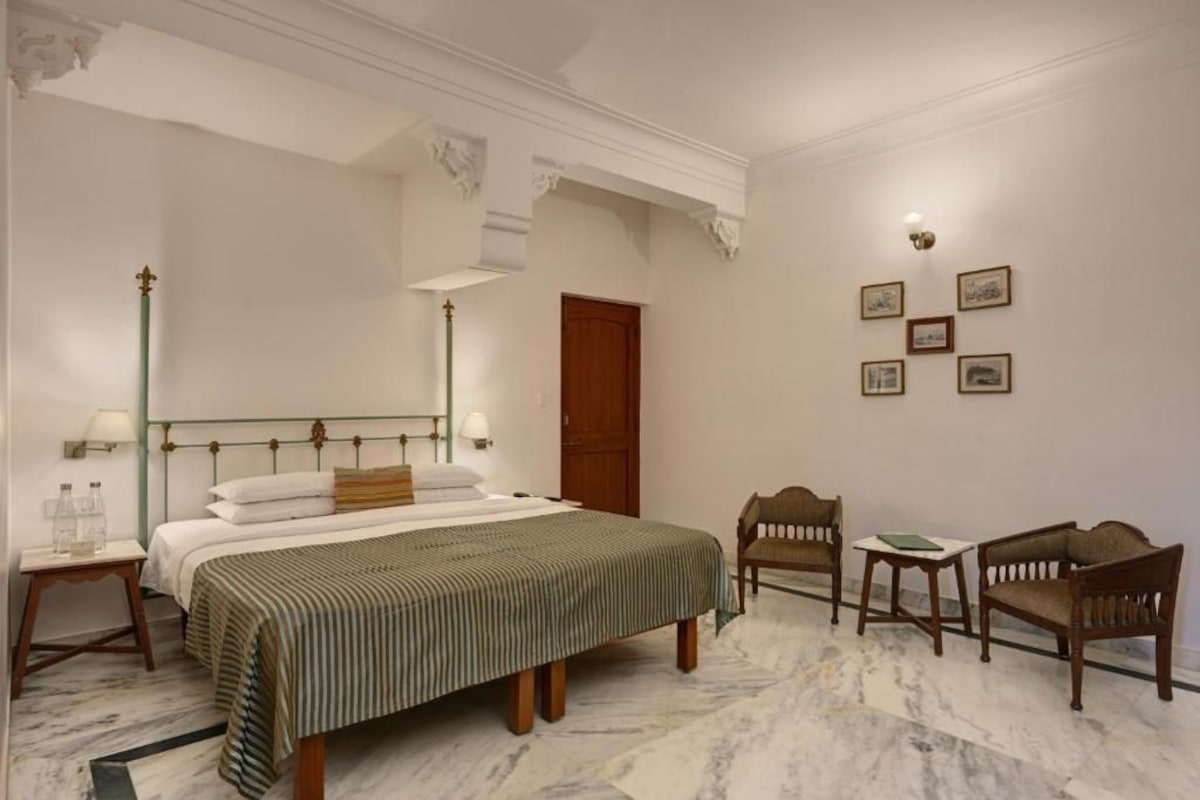 Une chambre d’hôtel avec un grand lit, une chaise en bois, une petite table et une porte.