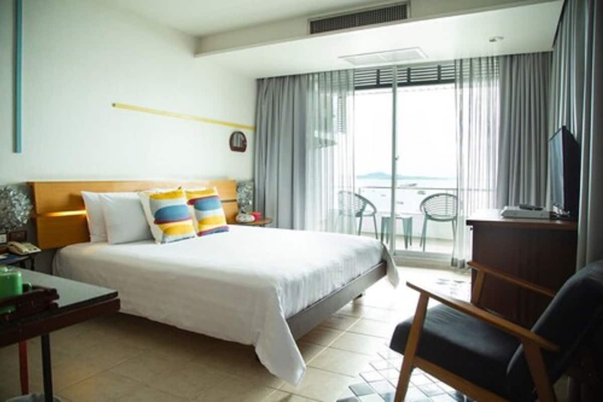A hotel room with a bed, a desk, a chair, a TV, and a balcony with a view.