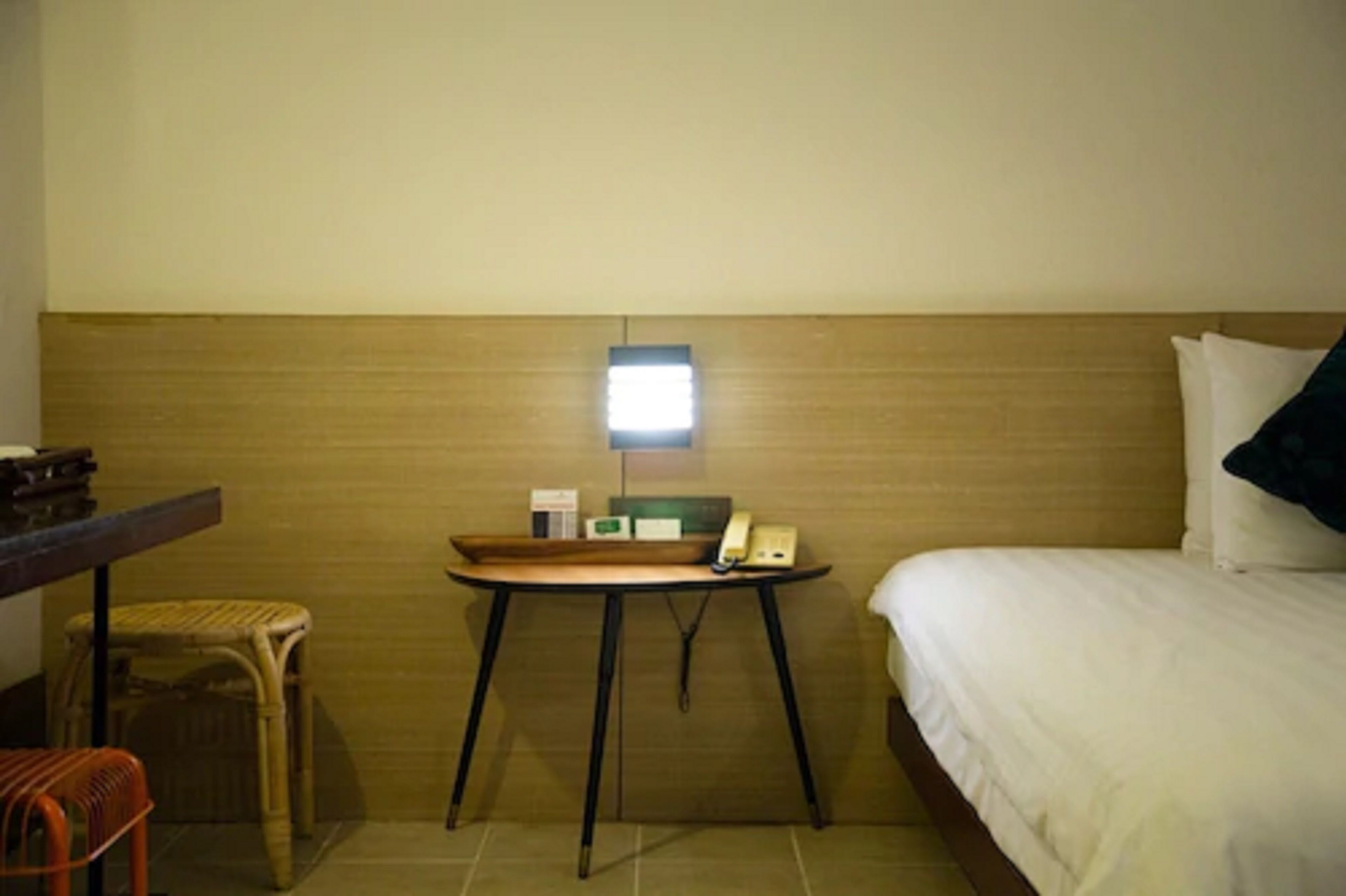 A hotel room with a bed, a small table with a telephone, a chair, and a nightstand.