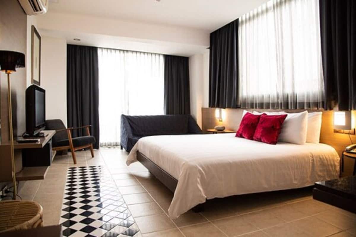 A hotel room with a large bed, a desk, a chair, a television, and a window with curtains.