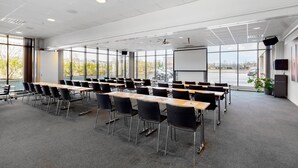 Un salón de conferencias con mesas, sillas, ventanas amplias y una pantalla para proyector.