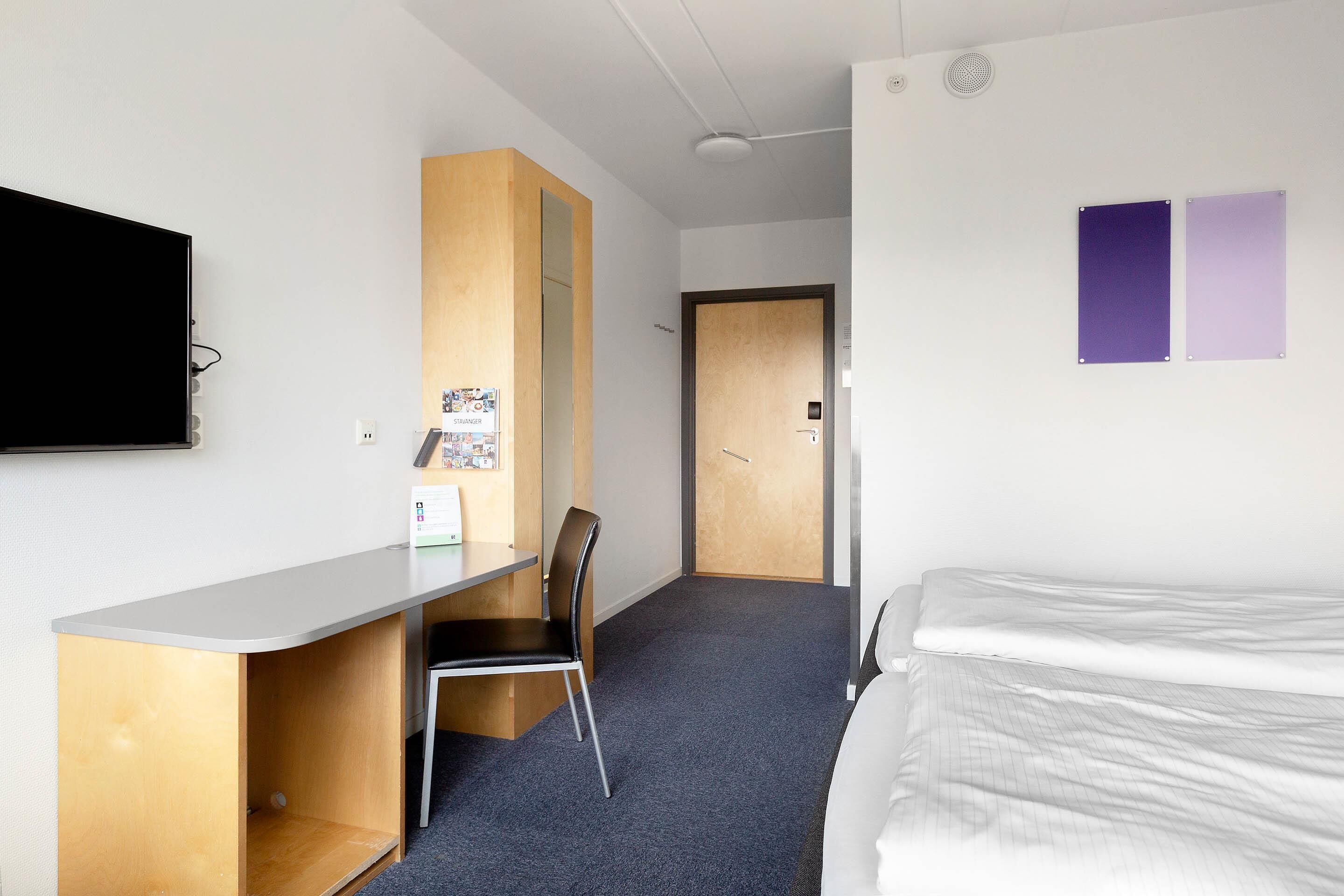 Une chambre d’hôtel avec un lit, un bureau, une chaise et un téléviseur.