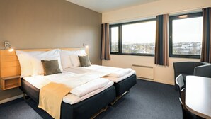 Habitación de hotel con cama, mesita de noche, silla y un gran ventanal con cortinas.