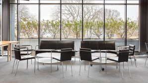 Un espacio interior moderno con ventanas amplias, una mesa redonda y sillas negras.