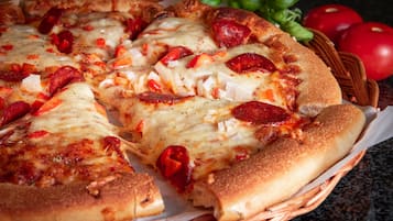 Una pizza con condimenti ben visibili e un cestino con pomodori e basilico.