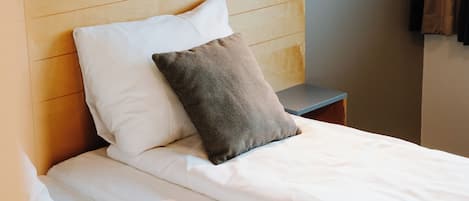Una cama bien hecha con sábanas blancas y dos almohadas, una mesita de noche con lámpara y un cabecero de madera.