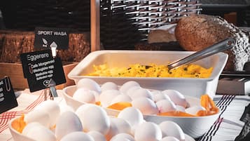 Een ontbijtbuffet met diverse gerechten, zoals eieren, worstjes, en een schaal roerei.