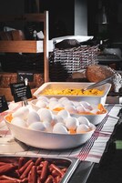 Een ontbijtbuffet met diverse gerechten, zoals eieren, worstjes, en een schaal roerei.