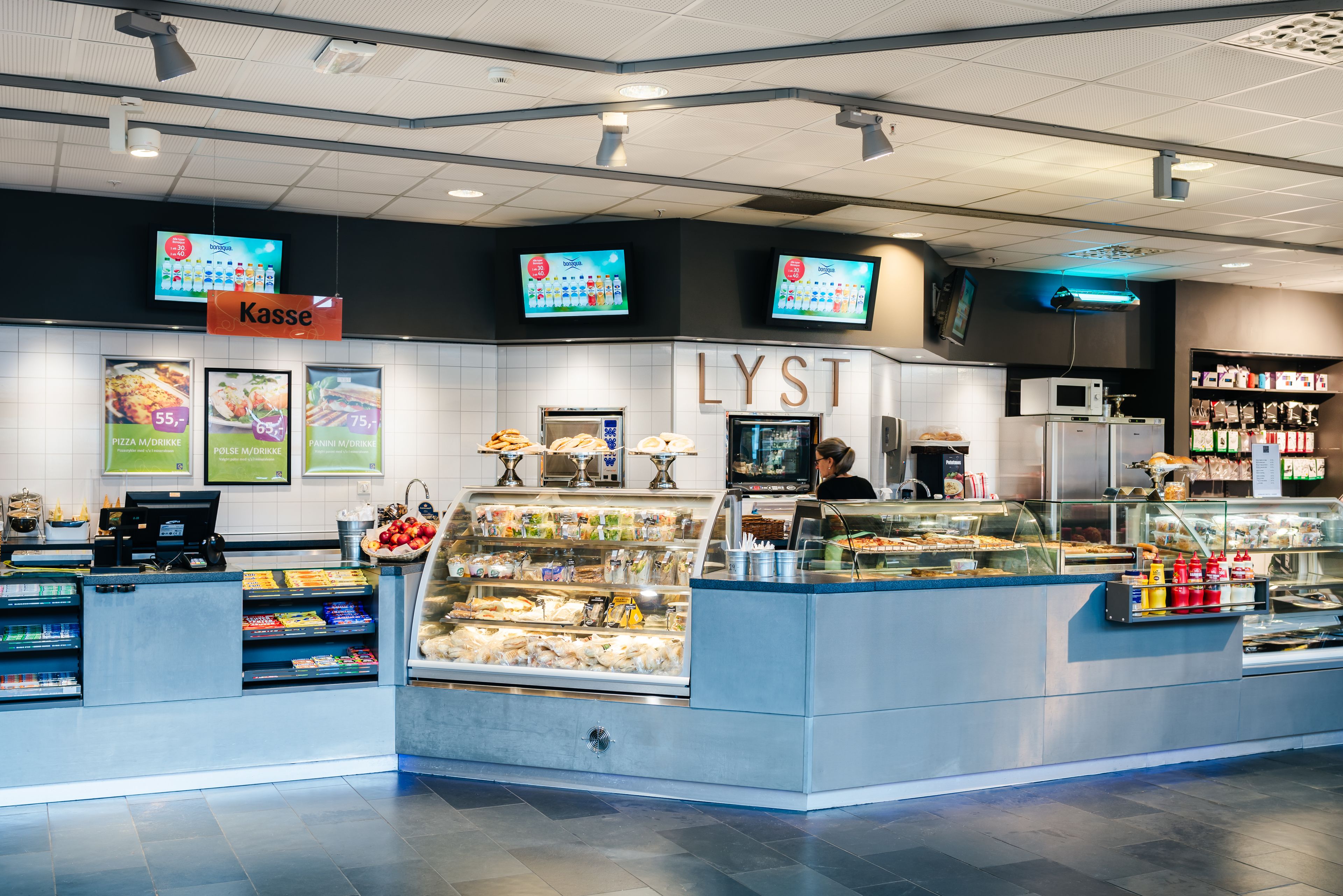 A food counter with a digital menu display, a refrigerated section, and a sign for 'Kasse'.
