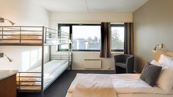 A hotel room with bunk beds, a single bed, a desk, a chair, and a large window with curtains.