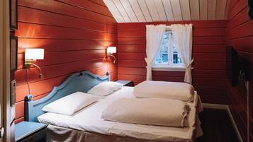Quarto com cama, mesa de cabeceira, janela com cortinas brancas e luminárias fixadas na parede.