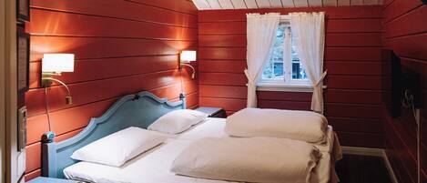 A room with a bed, a nightstand, a window with white curtains, and wall-mounted lights.