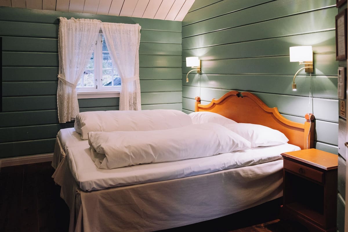 A single bed with white linens, a wooden headboard, and two wall-mounted bedside lamps.