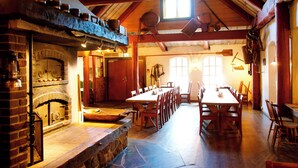 Un comedor rústico con una larga mesa de madera y sillas, una chimenea de piedra y un techo abovedado con vigas a la vista.