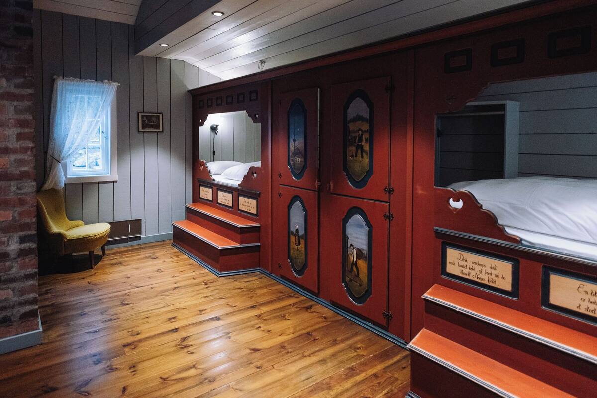 A room with a wooden floor, a single bed with a headboard, a chair, and a window with a curtain.