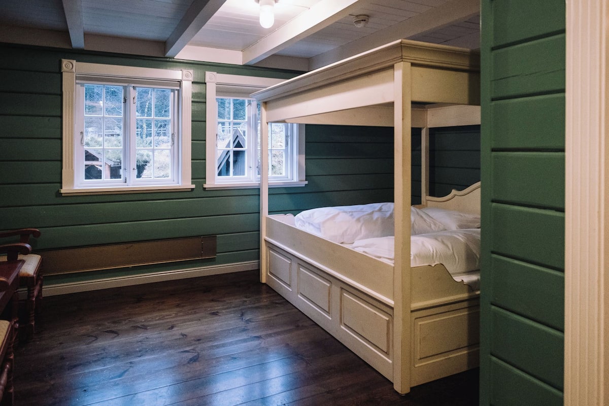 A room with a bunk bed, a window with a view of trees, and a wooden bench.