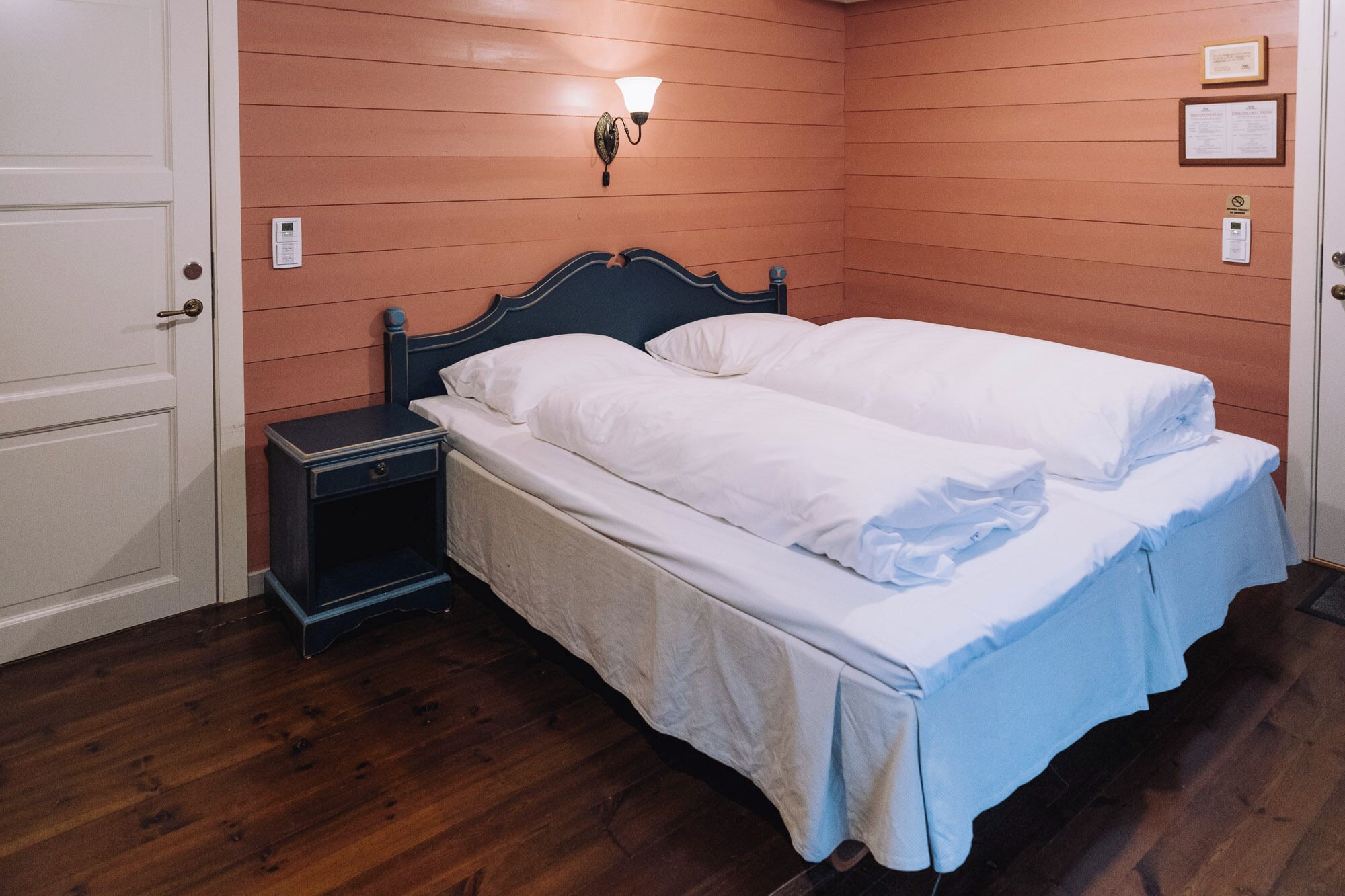 A double bed with white linens in a room with wooden panel walls and a nightstand.