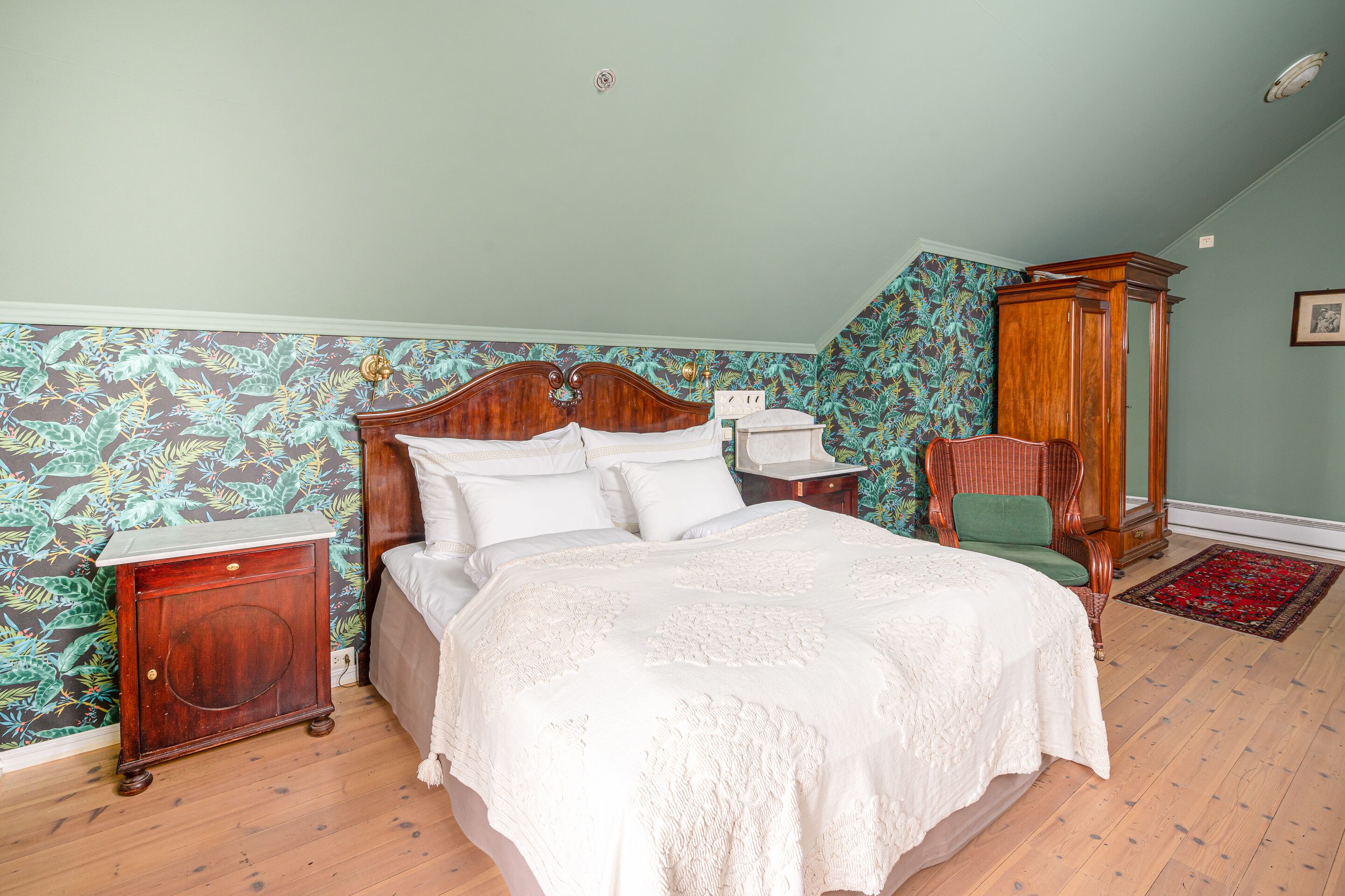 Un dormitorio con cama de madera, una mesita de noche, una silla verde y un armario de madera.