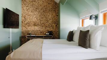 A hotel room with a bed, a TV mounted on the wall, a small table with a coffee maker, and a window with curtains.