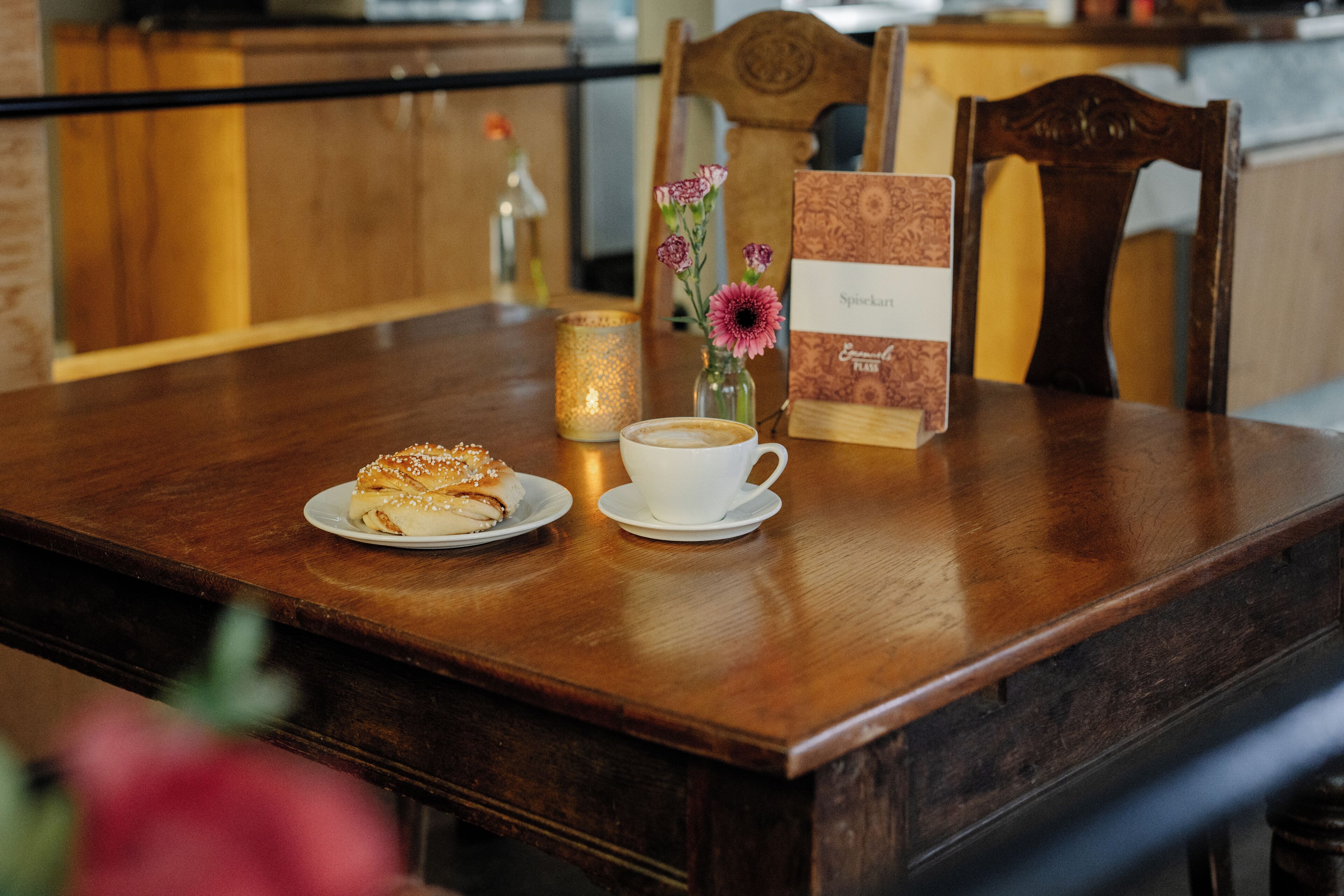 A wooden table with a plate of food, a cup of coffee, a candle, and a menu.