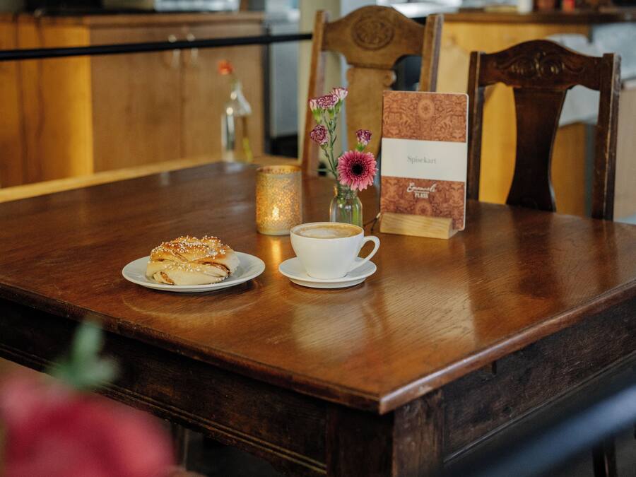 A wooden table with a plate of food, a cup of coffee, a candle, and a menu.
