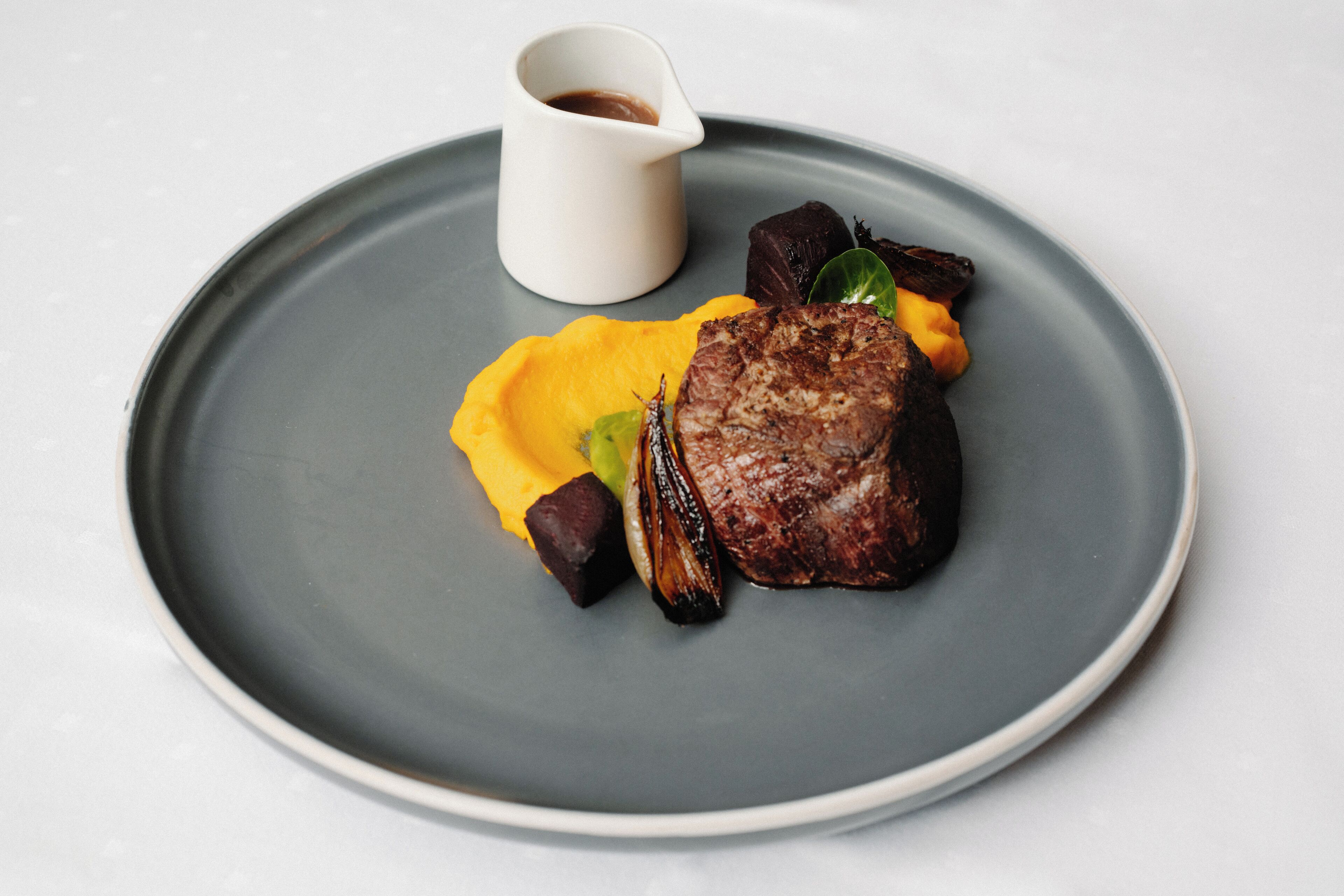 Une assiette contenant un steak, des légumes et une sauce.