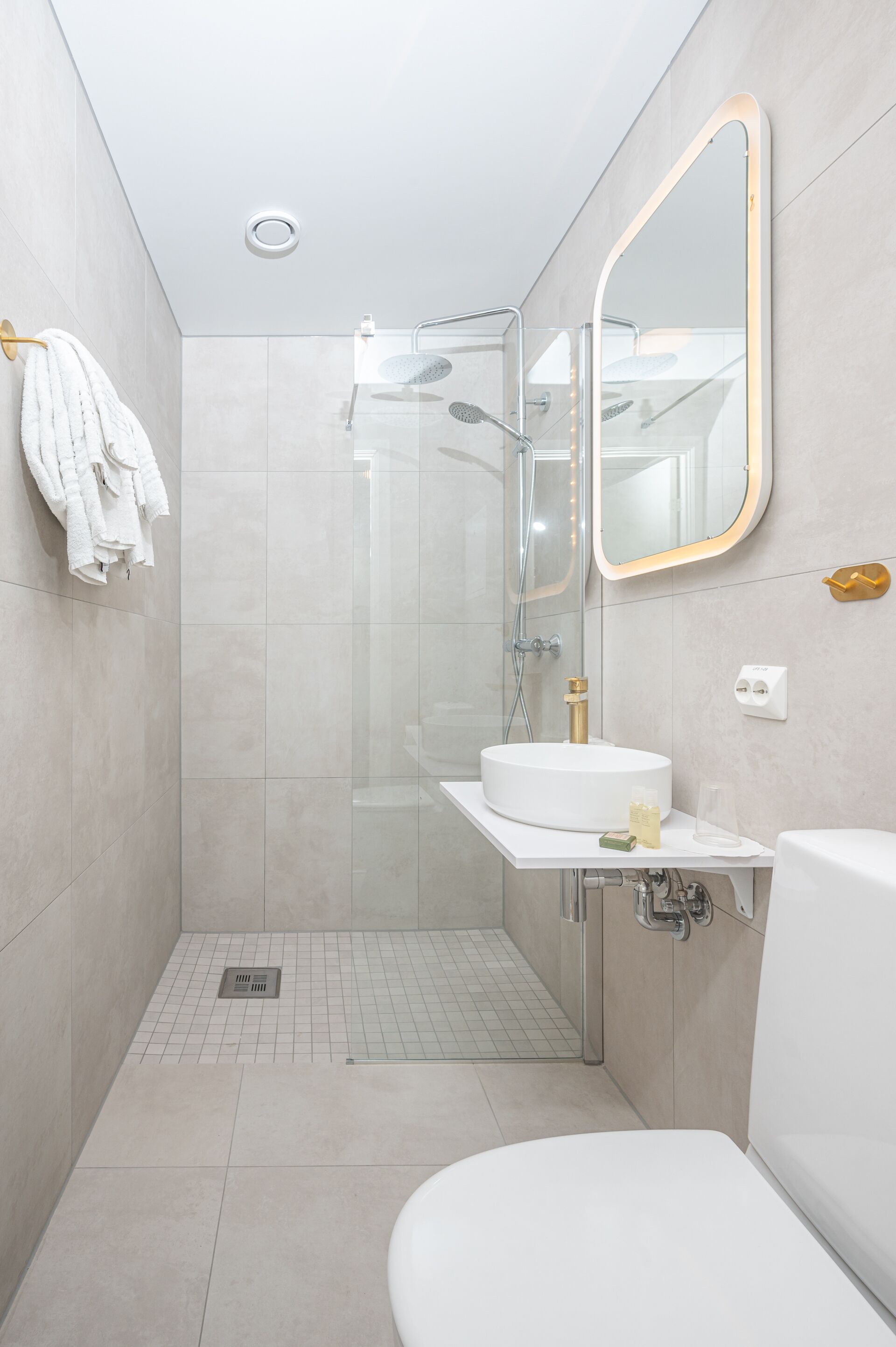 Un baño moderno con ducha envuelta en vidrio, un lavamanos blanco con detalles dorados y un espejo grande con marco dorado.