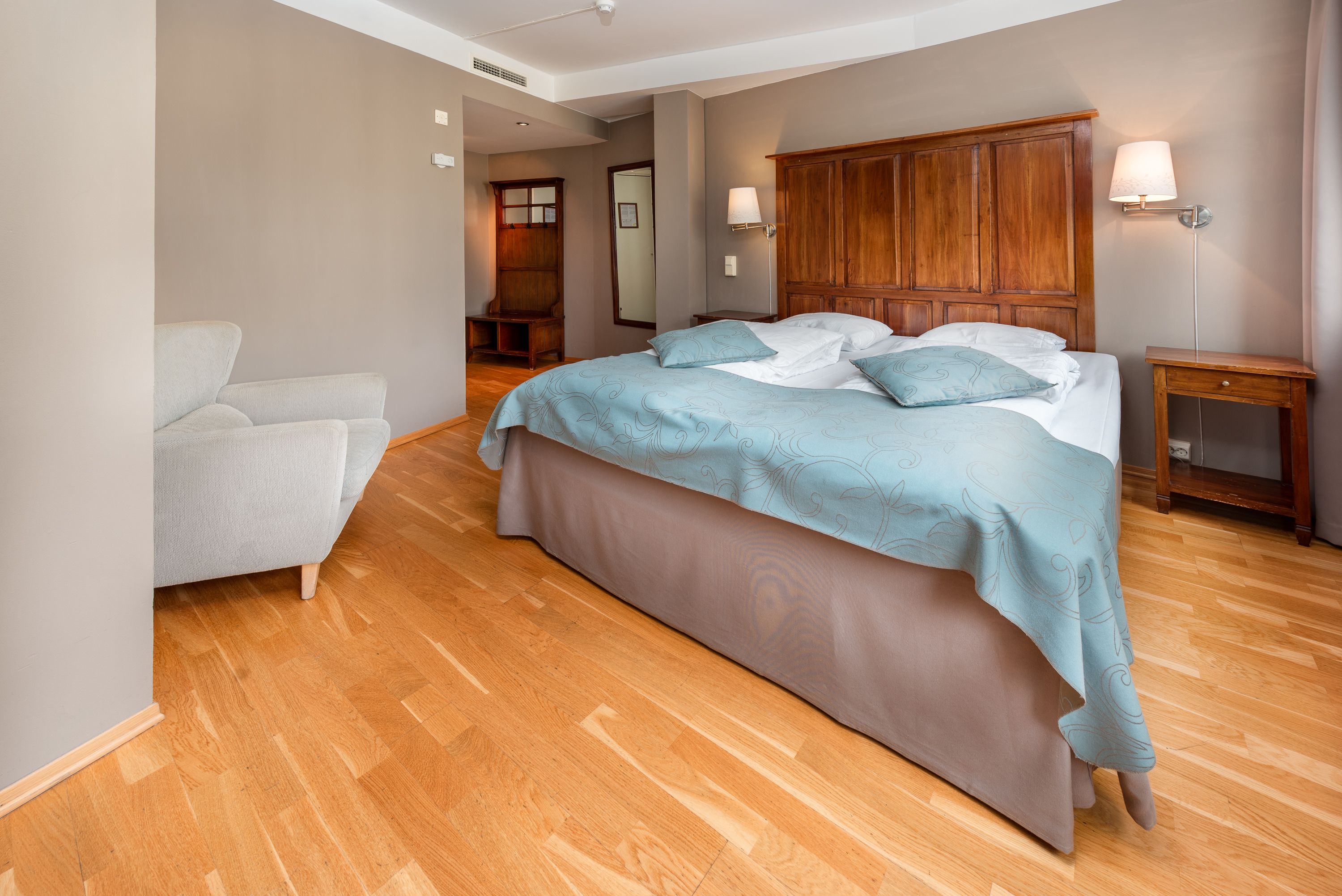 A bedroom with a large bed, a wooden wardrobe, a bedside table, and a chair.