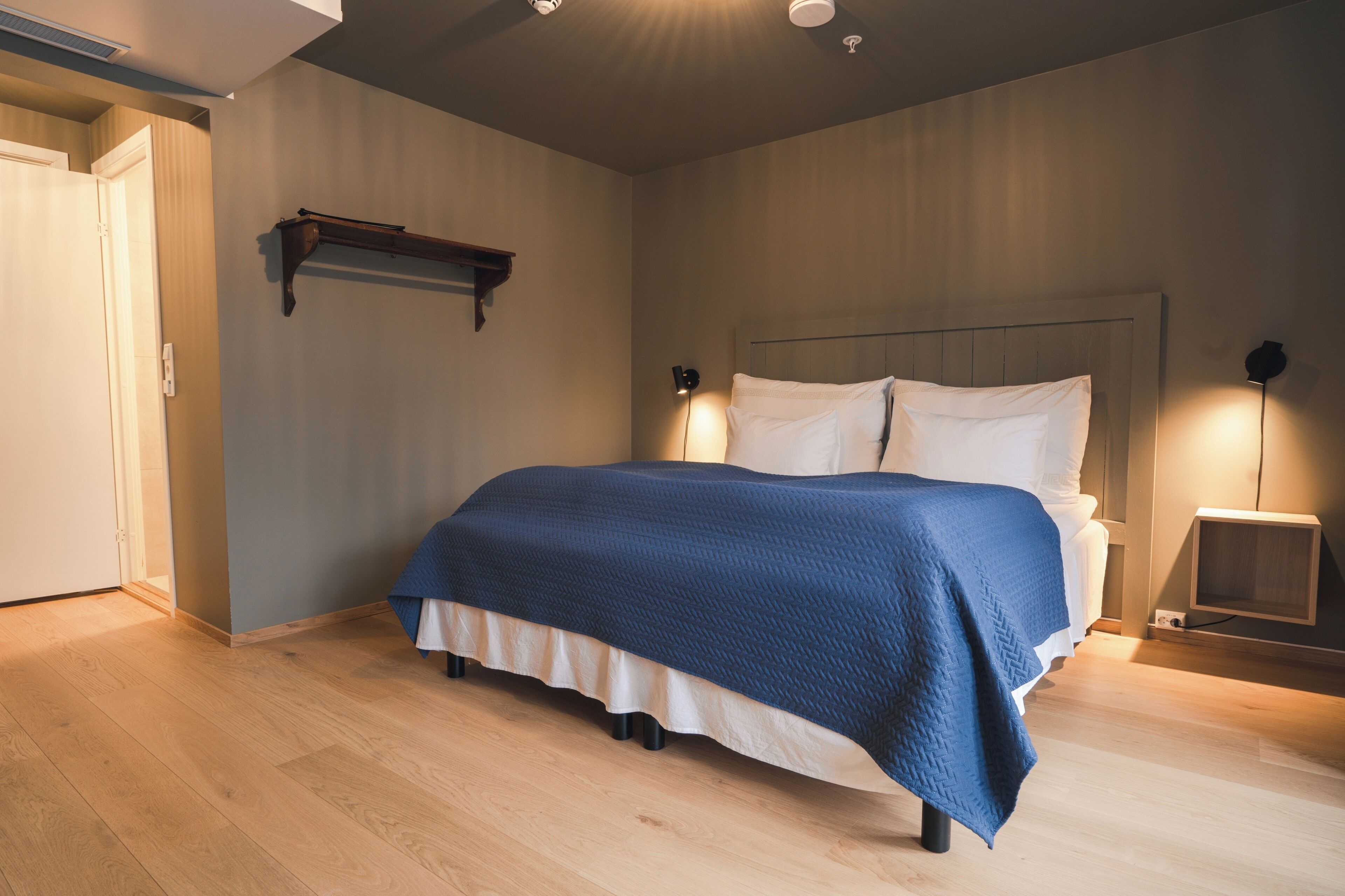 A bedroom with a bed, bedside lamps, a wooden floor, and a door.
