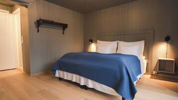 A bedroom with a bed, bedside lamps, a wooden floor, and a door.