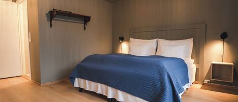 A bedroom with a bed, bedside lamps, a wooden floor, and a door.