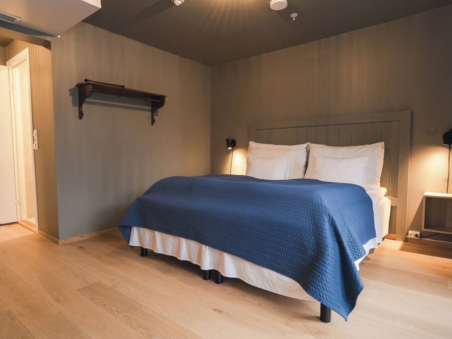 A bedroom with a bed, bedside lamps, a wooden floor, and a door.
